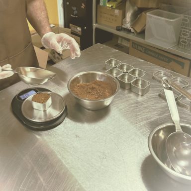 A person measuring cocoa powder in a kitchen with bowls and a digital scale.