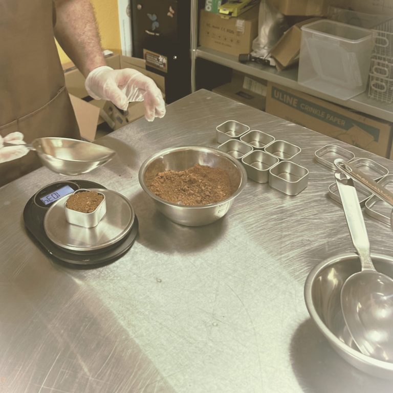 Lulu and GG's Grand Plan Foundation A person measures cocoa powder in a kitchen on a digital scale.