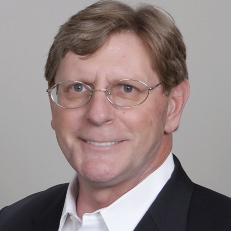 A professional man with glasses, wearing a dark suit and smiling warmly.